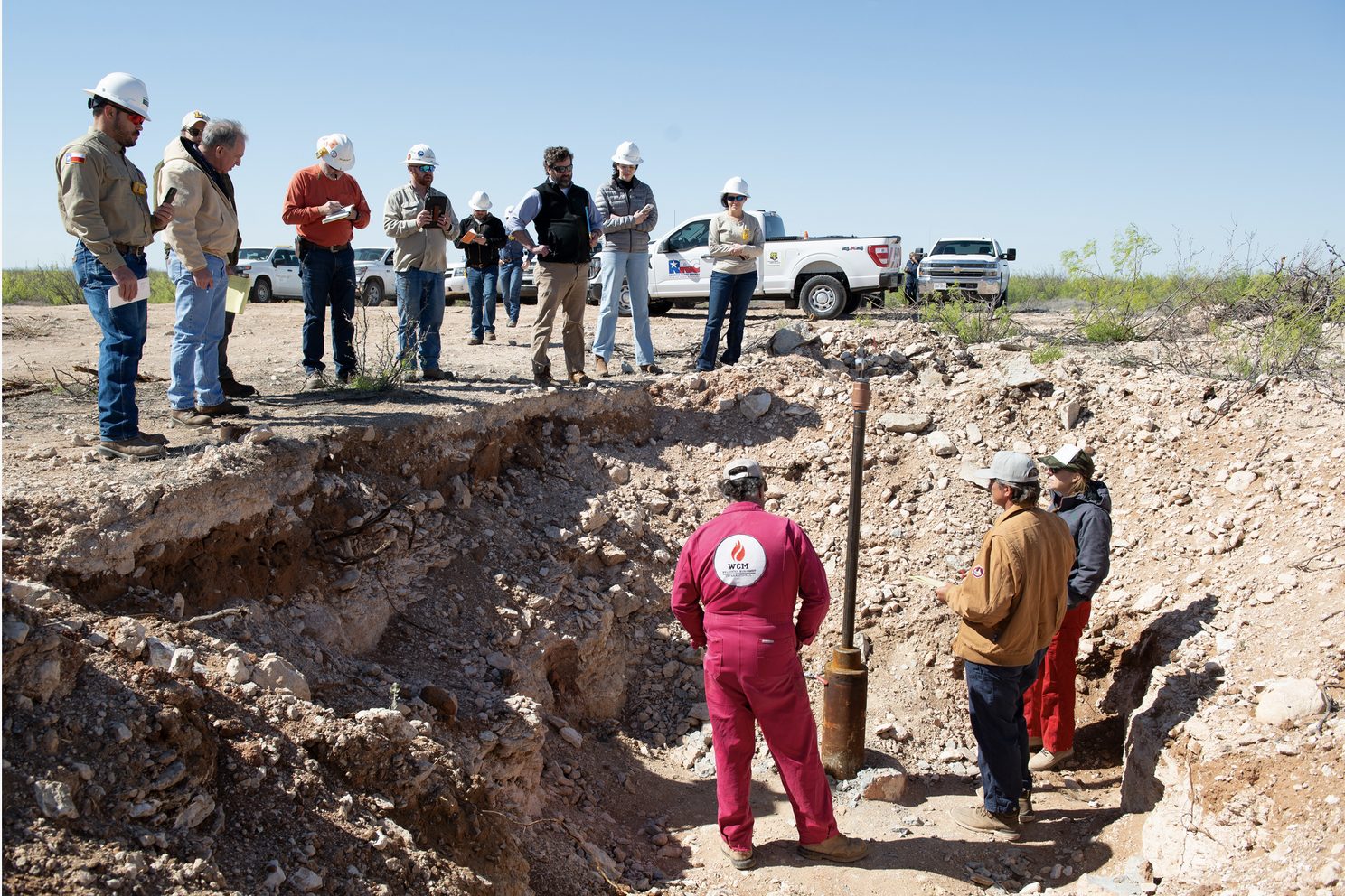 Contractors and attorneys for Chevron watch from above as Hawk Dunlap, Daniel Charest and Sarah Stogner (from left) inspect an excavated well on April 10 at Antina Ranch in Crane County, Texas. Credit: Mitch Borden/Marfa Public Radio